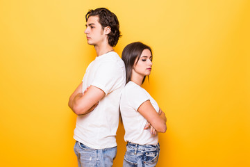 Wall Mural - Confused young couple standing with one another's back and looking at the camera with crossed arms over yellow background