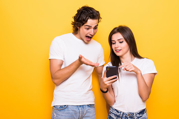 Wall Mural - Photo of positive excited people man and woman screaming and looking at each other while both using mobile phones isolated over yellow background