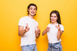 © F8  \ Suport Ukraine - Excited beautiful couple wearing white t-shirts standing isolated over yellow background, pointing at camera