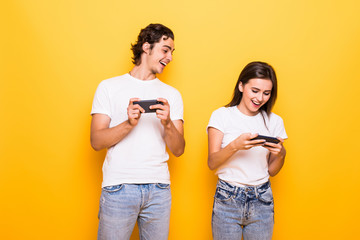 Sticker - Amusing young couple man and woman playing together video games on mobile phones isolated over yellow background