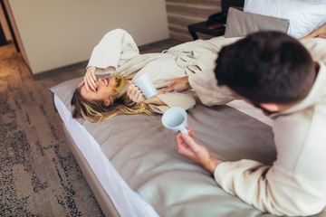 Couple in bathrobes lying on bed in hotel room.