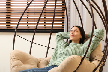 Poster - Young woman relaxing in hanging chair near window at home