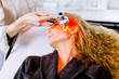 beautician doing red led light therapy to blond woman in beauty salon, facial photo therapy for skin pore cleansing. Anti-aging treatments and photo rejuvenation procedure, close up