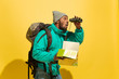 Full length portrait of a cheerful young african-american tourist guy with bag and map on yellow studio background Going to travel, looking for trip way, smiling and greeting. Crazy happy, astonished.