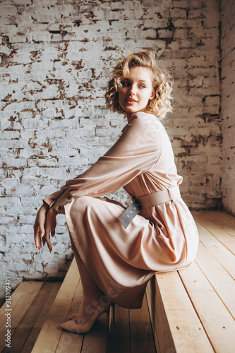 Photo: Portrait of an attractive curly blonde woman poses for the advertisement of a women's clothing store dressed in a light powder dress Portrait of an attractive curly blonde woman poses for the advertisement of a women's clothing store dressed in a light powder dress