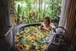 Young woman enjoying in outdoor luxury spa. Beautiful luxury stone bath tub with jungle view.Natural organic tropical ingredients in the water:ginger,lime,orange and sea salt. Beauty treatment concept