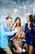 © vitaliymateha - Group of beautiful young people laughing, smiling and holding sparklers over silver shiny background. smartly dressed friends celebrating christmas or new year together, laughing and looking happy