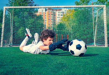 Wall Mural - Young soccer goalie attempting to make a save. little soccer goalkeeper with gloves. Kids - soccer champion. Boy goalkeeper in football sportswear on stadium with ball. Sport concept. Selective focus.