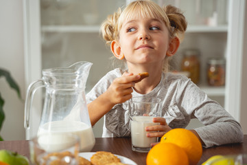 Adorable little girl holding cookie and glass of milk