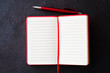 Empty red notebook with red pen on dark background. Blank paper for text.