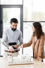 Wall Mural - smiling virtual reality architects talking and pointing with finger at model of house