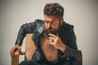 © Volodymyr - Brutal bearded fashionable man with serious face sitting in chair and looking at camera. Macho man Casanova attracting women. Sexy rich shirtless millionaire man with leather jacket.