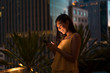 © Westend61 - Portrait of happy woman standing on roof terrace at dusk looking at cell phone