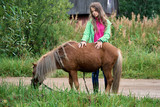 Teenage girl stands with a pony colt at countryside