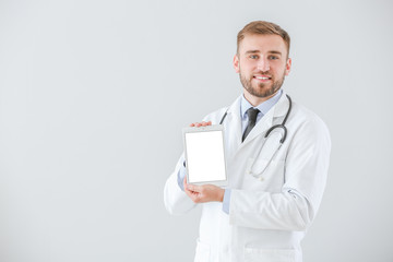 Wall Mural - Portrait of male doctor with tablet computer on light background