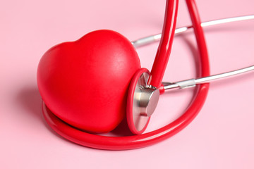 Modern stethoscope and red heart on color background, closeup