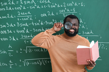 Wall Mural - African-American math teacher with book and magnifier near blackboard in classroom