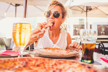 Beautiful adult caucasian woman eating italian food pizze - man couple point of view with beer and fresh drink on the table - people enjoying restaurant together sitting outdoor