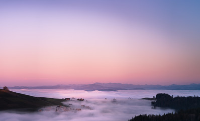 Canvas Print - panoramic view of a village in switzerland covered in fog after the sunset with warm colors