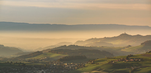 Wall Mural - a village covered in fog during sunset with warm light and a braodcast tower in the background