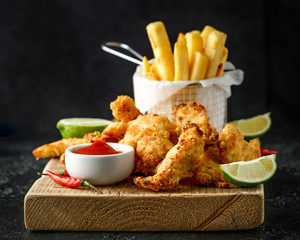 Wall Mural - Buttermilk chicken nuggets served on wooden board with potato chips, lime wedges and tomato ketchup