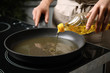 © New Africa - Woman pouring cooking oil from bottle into frying pan, closeup