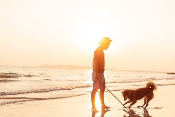 A man and a dog stand on the beach and sunset.