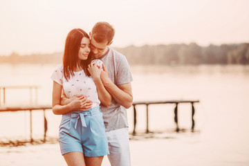 Loving young couple hugging on pier at sunset in summer.