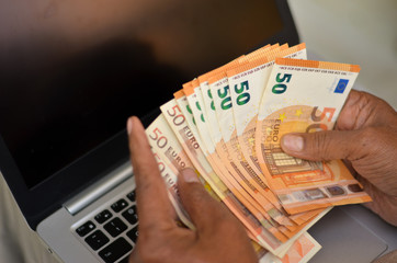 Hands of a rich man counting 50 euro bills or notes in front of a laptop screen. Euro is accepted in 19 countries forming Euro zone Concept shot - Foreign currency exchange and technology