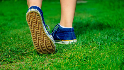 Walking women leg in jeans sneaker shoes on the road and green grass