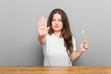 Wall Mural - Young plus size curvy woman holding a toothbrush standing with outstretched hand showing stop sign, preventing you.