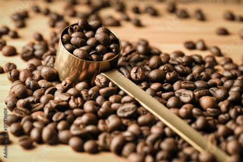 Fotografía Coffee beans are poured on a wooden surface and in the middle is a coffee spoon