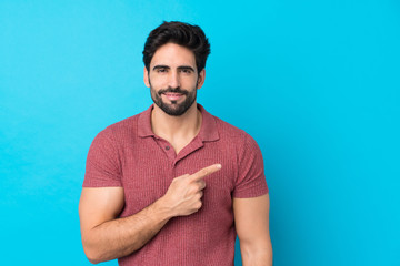 Young handsome man with beard over isolated blue background pointing to the side to present a product