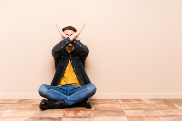 Young caucasian man sitting on the floor isolated keeping two arms crossed, denial concept.