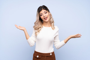 Wall Mural - Young teenager girl over isolated blue background holding copyspace with two hands