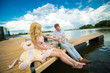 © Kate - Romantic date surprise. A young guy and a girl on a wooden pier. The guy opens the champagne.