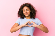Young African American Woman Against A Pink Background Smiling And Showing A Heart Shape With Hands.