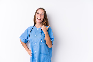 Wall Mural - Young nurse woman isolated points with thumb finger away, laughing and carefree.