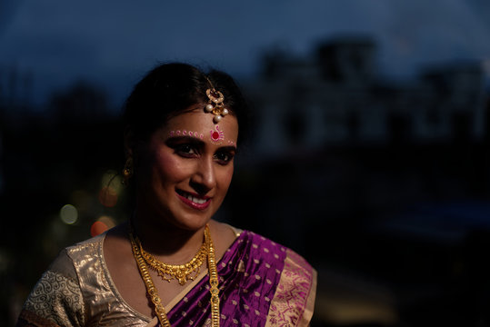 Portrait of a beautiful smiling brunette Indian Bengali bride in traditional sari standing on the roof top in evening. Indian lifestyle.