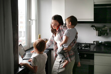 Busy Mom With Two Children Works On Laptop Kitchen