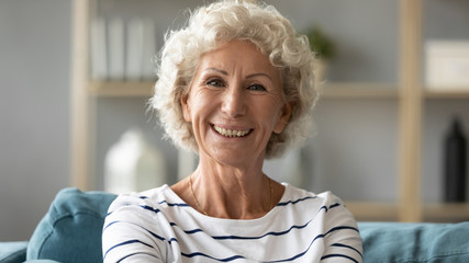 Headshot portrait elderly woman resting on couch looking at camera