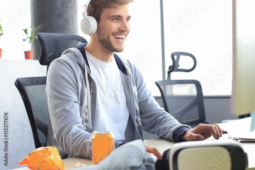 Fotografía Smiling young man in casual clothing using computer, streaming playthrough or walkthrough video