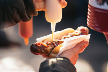 Woman pouring tomato sauce, mayonnaise and mustard on a grilled pork sausage Bratwurst at a German Market.