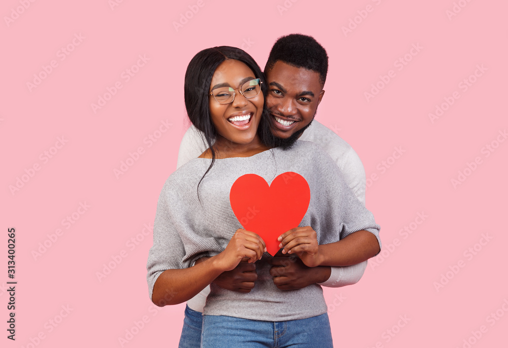 Joyful african couple holding big red heart together - obrazy, fototapety, plakaty 