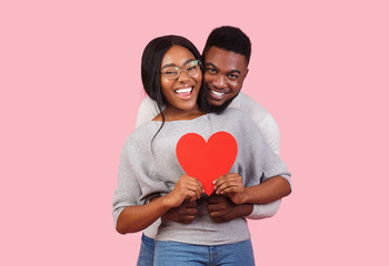 joyful african couple holding big red heart together