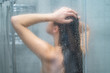 © Goffkein - Unfocused naked woman showering, bathing and washing long hair in shower under refreshing water jet at home