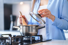 Woman Housewife Using Steel Metallic Saucepan For Preparing Dinner In The Kitchen At Home. Kitchenware For Cooking