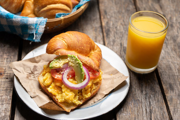 Canvas Print - Butter croissant bread with scrambled eggs and avocado on wooden background