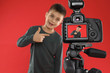 Cute little blogger recording video against red background, focus on camera