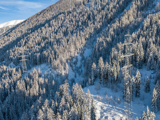 Wall Mural - Aerial view of power line through alpine valley in Switzerland. Snow covered trees in winter. Concept of power transmission.